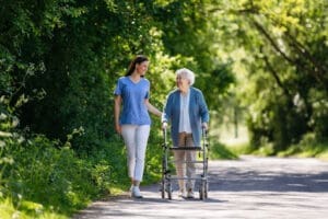 A young woman accompanies her elderly mother on a walk. The old woman uses a walker.