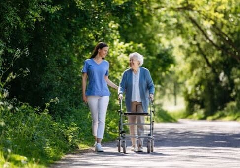 A young woman accompanies her elderly mother on a walk. The old woman uses a walker.