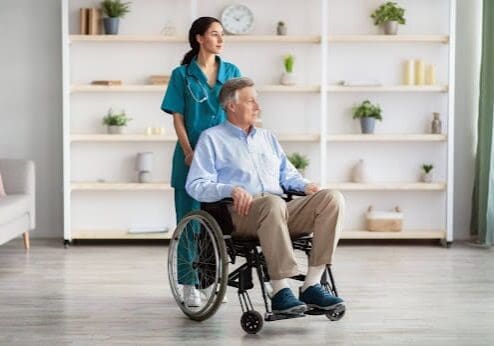 A nurse pushes an older gentleman around on a wheelchair.